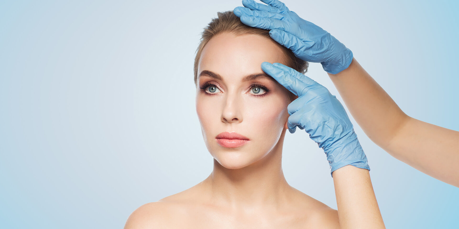 people, cosmetology, plastic surgery and beauty concept - surgeon or beautician hands touching woman face over blue background